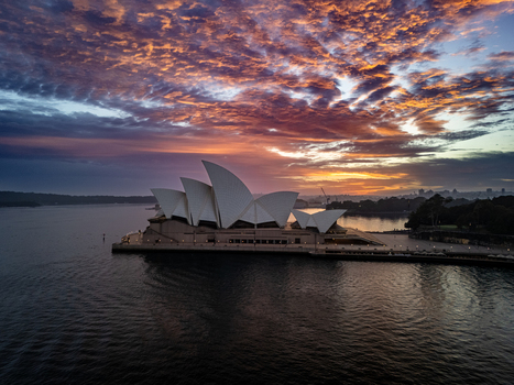 Aerial view of the iconic Sydney Opera House silhouetted against a vibrant fiery sunrise its white sails contrasting with the dark waters Sydney New South Wales Australia. Aerial view of the iconic Sydney Opera House silhouetted against a vibrant fiery sunrise its white sails contrasting with the dark waters Sydney New South Wales Australia.