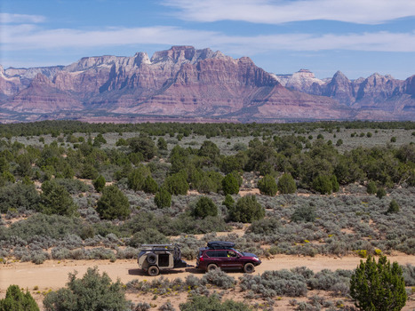 Aerial view of an SUV pulling a teardrop camper trailer on a dirt road on Gooseberry Mesa with Zion National Park cliffs in the background in Hurricane Utah United States. Aerial view of an SUV pulling a teardrop camper trailer on a dirt road on Gooseberry Mesa with Zion National Park cliffs in the background in Hurricane Utah United States.