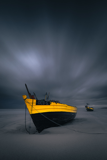 View of a traditional yellow and black fishing boat resting on the sand under a dramatic dark cloudy sky in Debki Pomeranian Voivodeship Poland. View of a traditional yellow and black fishing boat resting on the sand under a dramatic dark cloudy sky in Debki Pomeranian Voivodeship Poland.