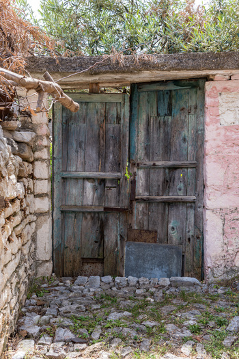 View of an old weathered wooden door with peeling blue paint set in a rustic stone wall along a cobblestone path in Qeparo Fshat Vlore County Albania. View of an old weathered wooden door with peeling blue paint set in a rustic stone wall along a cobblestone path in Qeparo Fshat Vlore County Albania.