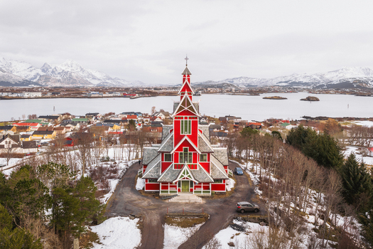 Aerial view of the vibrant red Buksnes Church stands out against the muted winter landscape with snow capped mountains in the distance Buksnes Kirke Nordland Norway. Aerial view of the vibrant red Buksnes Church stands out against the muted winter landscape with snow capped mountains in the distance Buksnes Kirke Nordland Norway.