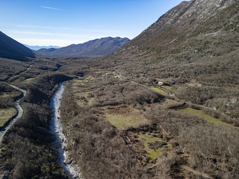 Aerial view of the river winding through the mountainous landscape with sparse winter vegetation rocky terrain and a winding road in Bzhete Markaj Qarku i Shkodres Albania. Aerial view of the river winding through the mountainous landscape with sparse winter vegetation rocky terrain and a winding road in Bzhete Markaj Qarku i Shkodres Albania.