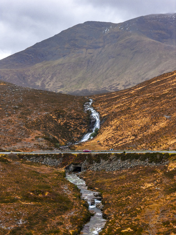 Aerial view of Eas a Bhradain waterfall cascading down a rugged hillside towards a road with a red car Isle of Skye Scotland United Kingdom. Aerial view of Eas a Bhradain waterfall cascading down a rugged hillside towards a road with a red car Isle of Skye Scotland United Kingdom.