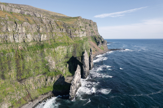 Aerial view of the dramatic cliffs of Hornstrandir Nature Reserve with green slopes meeting the blue ocean in Isafjordur Isafjardabaer Iceland. Aerial view of the dramatic cliffs of Hornstrandir Nature Reserve with green slopes meeting the blue ocean in Isafjordur Isafjardabaer Iceland.