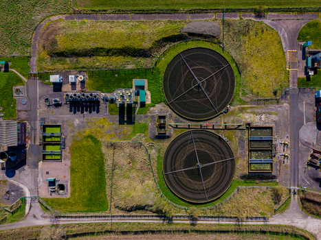 Aerial view of the Gnosall Heath wastewater treatment plant featuring large circular settling tanks and rectangular basins surrounded by green fields in Gnosall England United Kingdom. Aerial view of the Gnosall Heath wastewater treatment plant featuring large circular settling tanks and rectangular basins surrounded by green fields in Gnosall England United Kingdom.