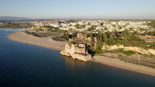Aerial view of Castelo de Sao Joao do Arade overlooking the sandy beach and the town of Ferragudo with calm blue water and clear sky in Ferragudo Faro District Portugal.