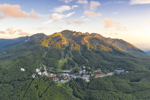 Aerial view of Cerreto Laghi mountain resort nestled in dense green forests and ski slopes under a golden sunset sky Cerreto Laghi Emilia Romagna Italy. Aerial view of Cerreto Laghi mountain resort nestled in dense green forests and ski slopes under a golden sunset sky Cerreto Laghi Emilia Romagna Italy.