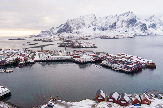 Aerial view of the fishing village of Lofoten with traditional red wooden cabins snow covered mountains and a bridge over the bay in Nordland Norway.