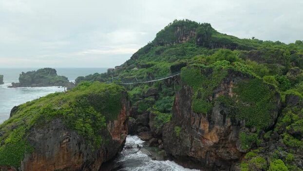 Aerial view of Siung Beach suspension bridge and cliffs Indonesia.