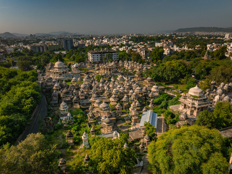 Aerial view of the historic Ahar Cenotaphs featuring numerous white marble domes and intricate stone structures surrounded by lush green trees in Udaipur Rajasthan India.