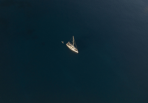Aerial view of a lone sailboat sailing on the deep blue Aegean Sea in Milos Greece. Aerial view of a lone sailboat sailing on the deep blue Aegean Sea in Milos Greece.