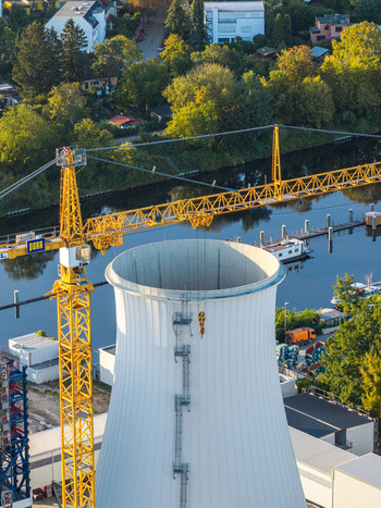 Aerial view of the cooling tower at Lichterfelde Power Station during deconstruction with a yellow construction crane river and surrounding greenery in Berlin Berlin Germany. Aerial view of the cooling tower at Lichterfelde Power Station during deconstruction with a yellow construction crane river and surrounding greenery in Berlin Berlin Germany.