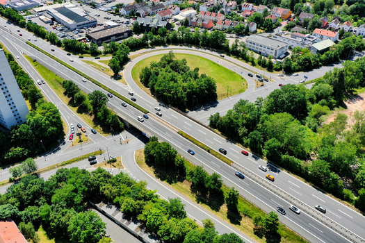 Aerial view of the A73 motorway interchange with cars driving past green trees and urban buildings in Nurnberg Bayern Germany. Aerial view of the A73 motorway interchange with cars driving past green trees and urban buildings in Nurnberg Bayern Germany.
