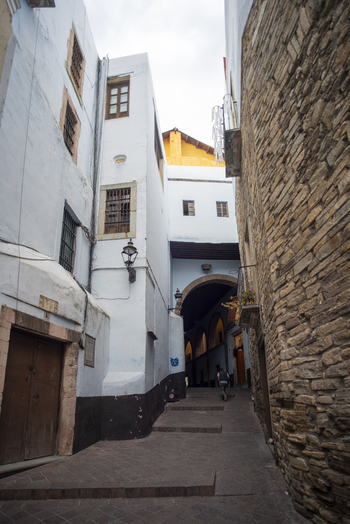 View of a narrow historic alleyway with white washed walls stone masonry and a person walking towards an arched passage in Guanajuato Guanajuato Mexico. View of a narrow historic alleyway with white washed walls stone masonry and a person walking towards an arched passage in Guanajuato Guanajuato Mexico.