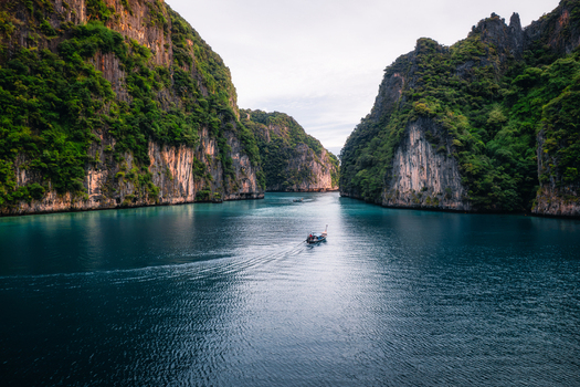 Aerial view of Pi Leh Bay featuring towering limestone cliffs and turquoise water with a traditional long tail boat navigating the calm sea in Tambon Ao Nang Chang Wat Krabi Thailand. Aerial view of Pi Leh Bay featuring towering limestone cliffs and turquoise water with a traditional long tail boat navigating the calm sea in Tambon Ao Nang Chang Wat Krabi Thailand.