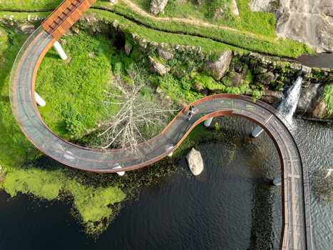 Aerial view of the Acude da Ribeira winding walkway over a river surrounded by lush green vegetation and rocky terrain in Ervedal Coimbra Portugal. Aerial view of the Acude da Ribeira winding walkway over a river surrounded by lush green vegetation and rocky terrain in Ervedal Coimbra Portugal.