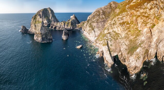 Aerial view of Glenlough Bay featuring dramatic sea cliffs rugged rock formations rising from the Atlantic Ocean and grassy slopes in Ardara County Donegal Ireland.