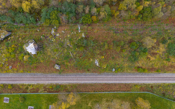 Aerial view of a railway track running through a landscape with scattered rocks autumn trees and green grass in Andalsnes More og Romsdal Norway.