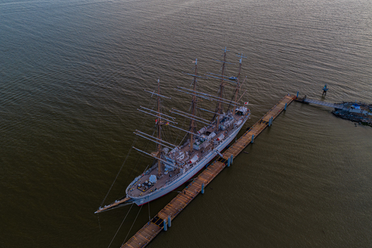 Aerial view of a large white tall ship docked at a wooden pier in the harbour of Vancouver British Columbia Canada.