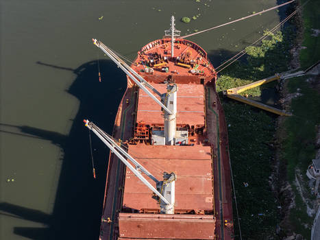 Aerial view of a large cargo ship moored on the Rio Ozama with cranes on deck and shadows cast on the water in Santo Domingo Santo Domingo Dominican Republic.