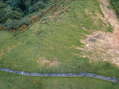 Aerial view of a winding asphalt path with parked vehicles traversing a vibrant green hillside contrasting with dense forest and reddish earth Obudu Cross River Nigeria.