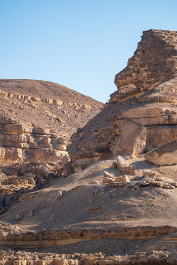 View of sun drenched jagged rocky cliffs casting shadows on the sandy ground under a clear blue sky Wadi Degla Protectorate Cairo Egypt. View of sun drenched jagged rocky cliffs casting shadows on the sandy ground under a clear blue sky Wadi Degla Protectorate Cairo Egypt.
