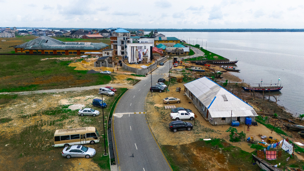 Aerial view of a coastal town featuring a road parked cars residential buildings and wooden boats moored along the riverbank in Minima Rivers Nigeria.
