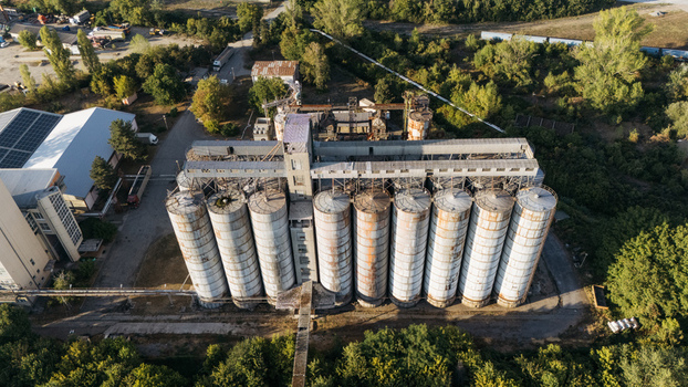 Aerial view of industrial grain silos with weathered metal surfaces surrounded by lush green trees and vegetation in Sremska Mitrovica Vojvodina Serbia. Aerial view of industrial grain silos with weathered metal surfaces surrounded by lush green trees and vegetation in Sremska Mitrovica Vojvodina Serbia.