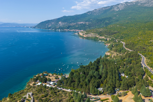 Aerial view of Lake Ohrid with its deep blue waters forested shoreline small boats and a coastal road winding along the mountainside in Ohrid Municipality of Ohrid North Macedonia.