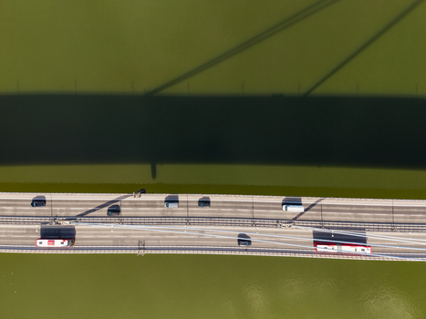 Aerial view of vehicles driving across a bridge over the green waters of the Danube River with a large shadow cast on the surface in Bratislava Bratislava Region Slovakia. Aerial view of vehicles driving across a bridge over the green waters of the Danube River with a large shadow cast on the surface in Bratislava Bratislava Region Slovakia.