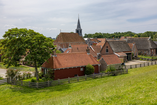 View of traditional brick houses with red tiled roofs a church spire and lush green fields in the historic village of Moddergat Friesland Netherlands. View of traditional brick houses with red tiled roofs a church spire and lush green fields in the historic village of Moddergat Friesland Netherlands.