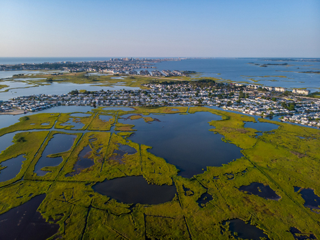 Ocean City United States 28 July 2019 Aerial view of marshlands and coastal waterways with residential areas in the distance under a clear blue sky.