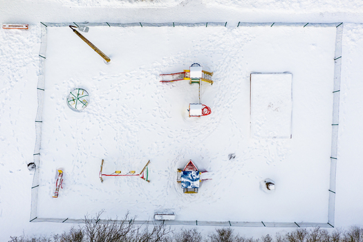 Aerial view of a snow covered playground featuring a slide a merry go round a swing set and a sandbox surrounded by a fence in Latvia. Aerial view of a snow covered playground featuring a slide a merry go round a swing set and a sandbox surrounded by a fence in Latvia.