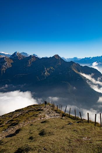 View of the Swiss Alps with a person walking along a mountain trail lined with wooden fence posts above a sea of clouds in Airolo Ticino Switzerland. View of the Swiss Alps with a person walking along a mountain trail lined with wooden fence posts above a sea of clouds in Airolo Ticino Switzerland.