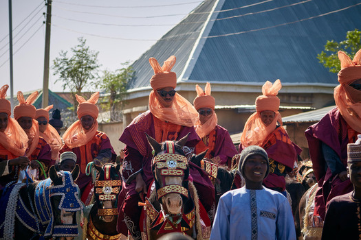 Zaria city Nigeria 21 March 2026 View of a vibrant procession where rich orange and deep crimson traditional attire gleams as riders on adorned animals parade under a bright sky. Zaria city Nigeria 21 March 2026 View of a vibrant procession where rich orange and deep crimson traditional attire gleams as riders on adorned animals parade under a bright sky.