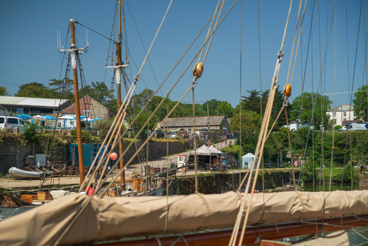 View of historic tall ship masts and rigging at the harbour with stone buildings and clear blue sky in Charlestown Cornwall United Kingdom. View of historic tall ship masts and rigging at the harbour with stone buildings and clear blue sky in Charlestown Cornwall United Kingdom.