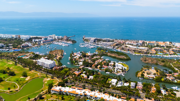 Aerial view of a vibrant coastal scene with turquoise waters meeting sandy shores dotted with yachts and lush green landscapes Nuevo Vallarta Mexico.