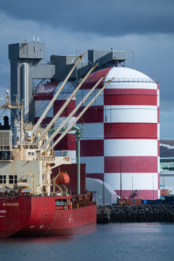 Hafnarfjordur Iceland 17 April 2026 View of a large red cargo ship docked at the port next to industrial red and white checkered silos under a cloudy sky.
