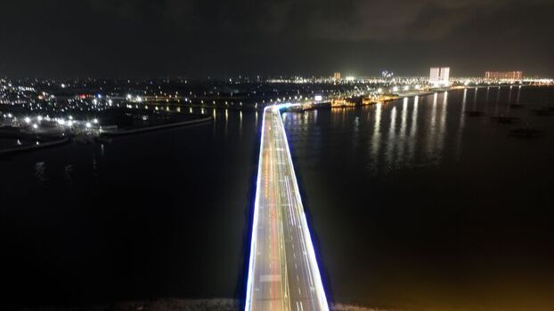 Aerial view of the illuminated bridge at Pantai Indah Kapuk 2 with vibrant light trails from night traffic over the calm water in Kecamatan Penjaringan Banten Indonesia. Aerial view of the illuminated bridge at Pantai Indah Kapuk 2 with vibrant light trails from night traffic over the calm water in Kecamatan Penjaringan Banten Indonesia.