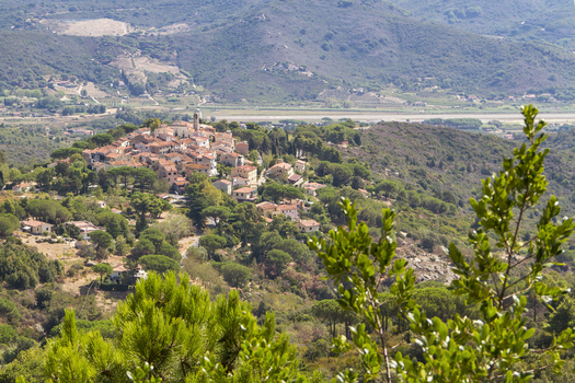 View of a quaint hilltop village with terracotta roofs nestled amidst lush green trees and rolling hills under a bright sky Elba Tuscany Italy. View of a quaint hilltop village with terracotta roofs nestled amidst lush green trees and rolling hills under a bright sky Elba Tuscany Italy.