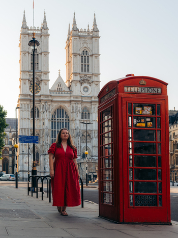 View of a woman in a vivid red dress by an iconic red telephone booth contrasting with the grand Westminster Abbey London England United Kingdom. View of a woman in a vivid red dress by an iconic red telephone booth contrasting with the grand Westminster Abbey London England United Kingdom.