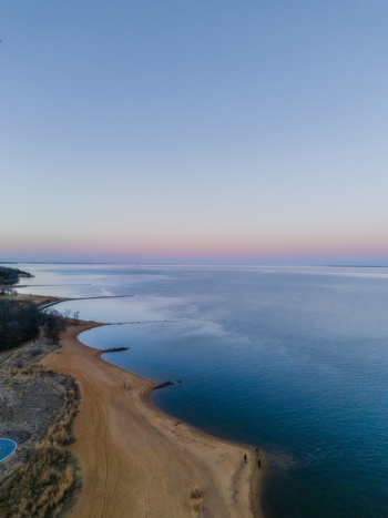 Aerial view of the sandy coastline at Sandy Point State Park with calm blue water and a soft pink horizon at dusk in Annapolis Maryland United States. Aerial view of the sandy coastline at Sandy Point State Park with calm blue water and a soft pink horizon at dusk in Annapolis Maryland United States.