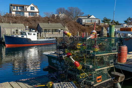 View of fishing boats and stacked lobster traps on a wooden dock with coastal houses in the background at Martha s Vineyard Edgartown Massachusetts United States.