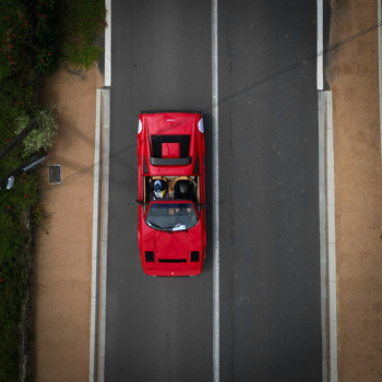 Aerial view of a red vintage sports car driving on an asphalt road with two people inside in La Chapelle de Guinchay Bourgogne Franche Comte France.