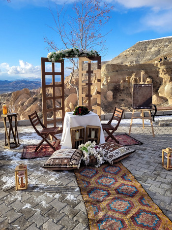 View of a romantic outdoor proposal setup with a wooden arch and floral decorations overlooking the unique rock formations and snowy hills under a bright blue sky Turkiye. View of a romantic outdoor proposal setup with a wooden arch and floral decorations overlooking the unique rock formations and snowy hills under a bright blue sky Turkiye.
