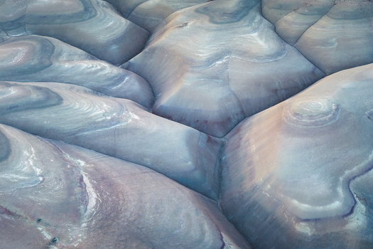 Aerial view of undulating layered rock formations create a mesmerizing tapestry of pale blues purples and creams carved by time and weather Hanksville Utah United States. Aerial view of undulating layered rock formations create a mesmerizing tapestry of pale blues purples and creams carved by time and weather Hanksville Utah United States.