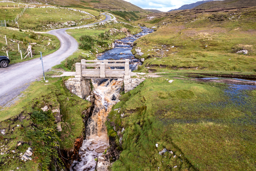 Aerial view of the historic stone bridge at An Port spanning a cascading waterfall in the rugged landscape of Ardara County Donegal Ireland.