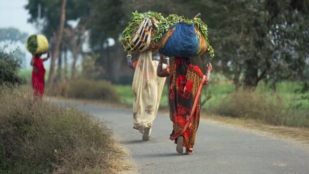 View of women carrying bundles on their heads on a rural road India.