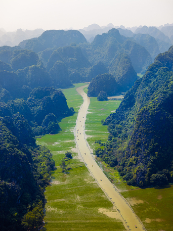 Aerial view of a winding river flowing through vibrant green rice paddies nestled between towering karst limestone mountains in the rural landscape of Vietnam. Aerial view of a winding river flowing through vibrant green rice paddies nestled between towering karst limestone mountains in the rural landscape of Vietnam.