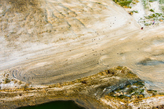 Aerial view of sandy riverbank with tire tracks sparse vegetation and birds flying over the landscape in Rajshahi Rajshahi Division Bangladesh.